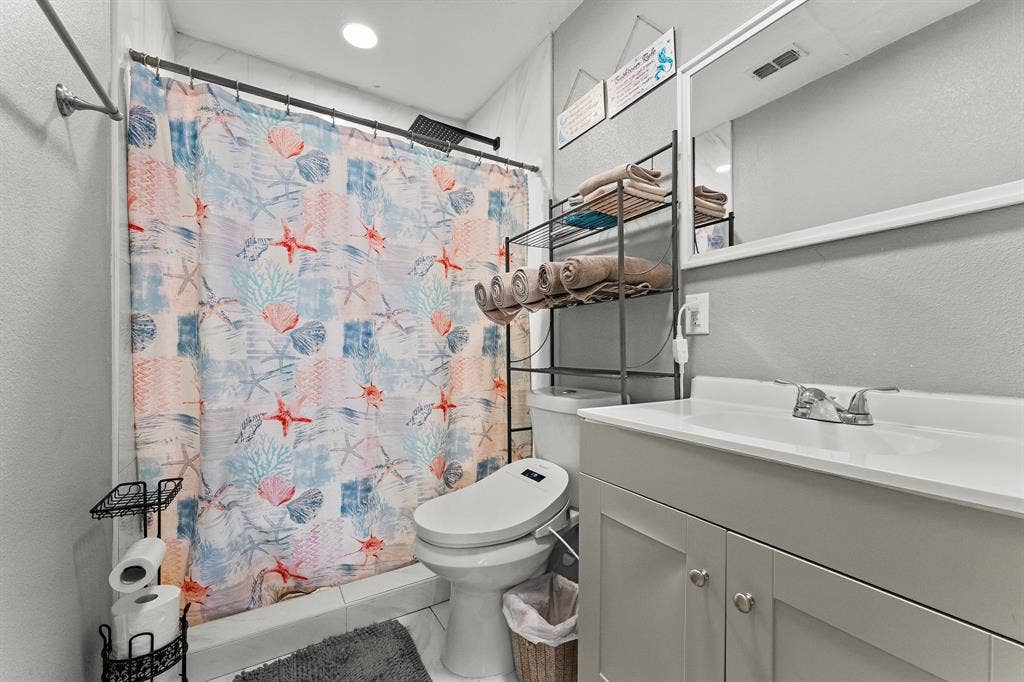 Grey shaker-style vanity with a solid-surface integrated countertop, two-handle chrome faucet, rectangular wall-mounted mirror, and recessed ceiling lighting