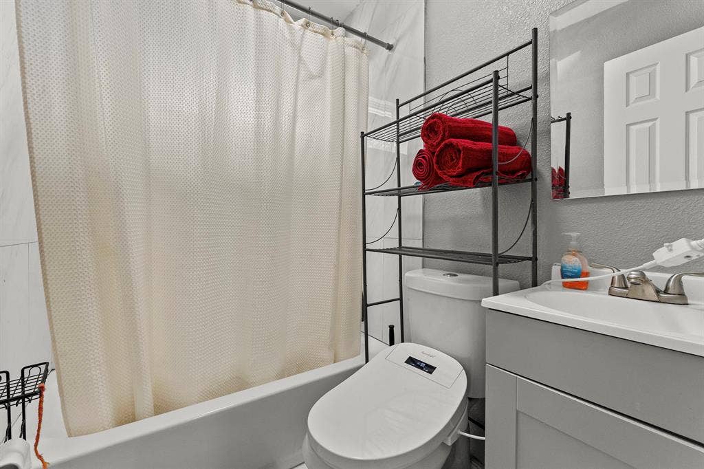Bathroom featuring a bathtub with a shower enclosure, white vanity cabinet with an integrated basin, metal dual-handle faucet, and frameless wall-mounted mirror