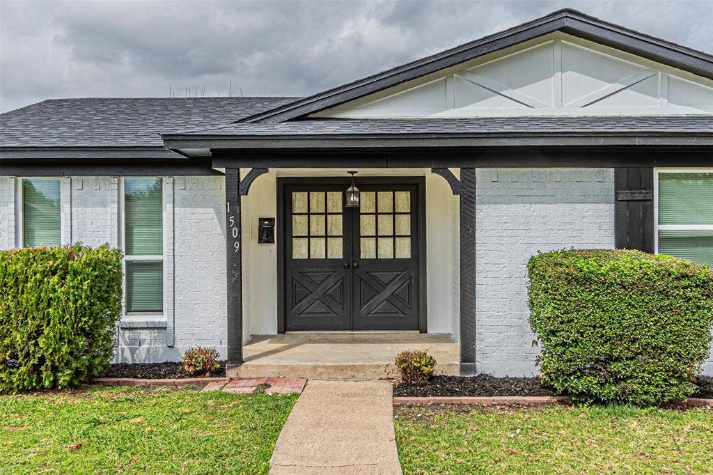 1509 Crockett Street, Garland, TX 75042 Painted brick exterior featuring decorative gable trim, double-door entrance with X-panel detailing, multi-pane glass inserts, and a covered front porch