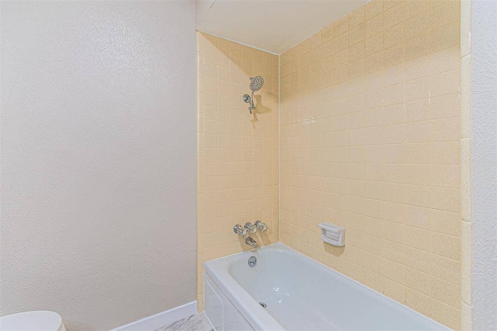 1509 Crockett Street, Garland, TX 75042 Bathtub with integrated shower, wall-mounted metallic fixtures, and tiled wall surround