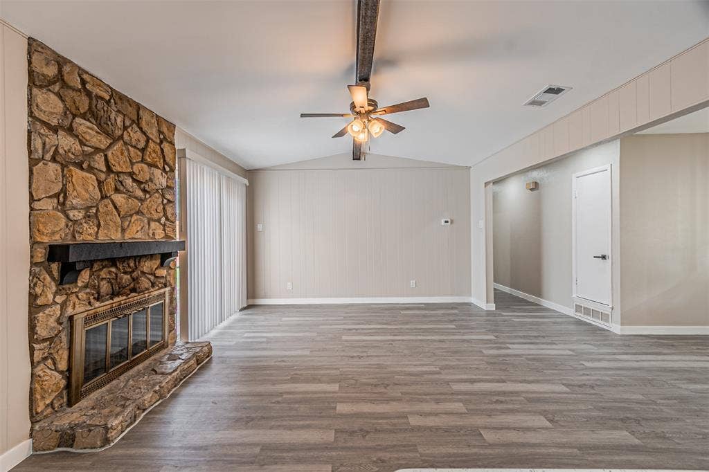 1509 Crockett Street, Garland, TX 75042 Living area featuring wood-finish flooring, a vaulted ceiling, floor-to-ceiling stone fireplace with a prominent mantel, and sliding glass doors