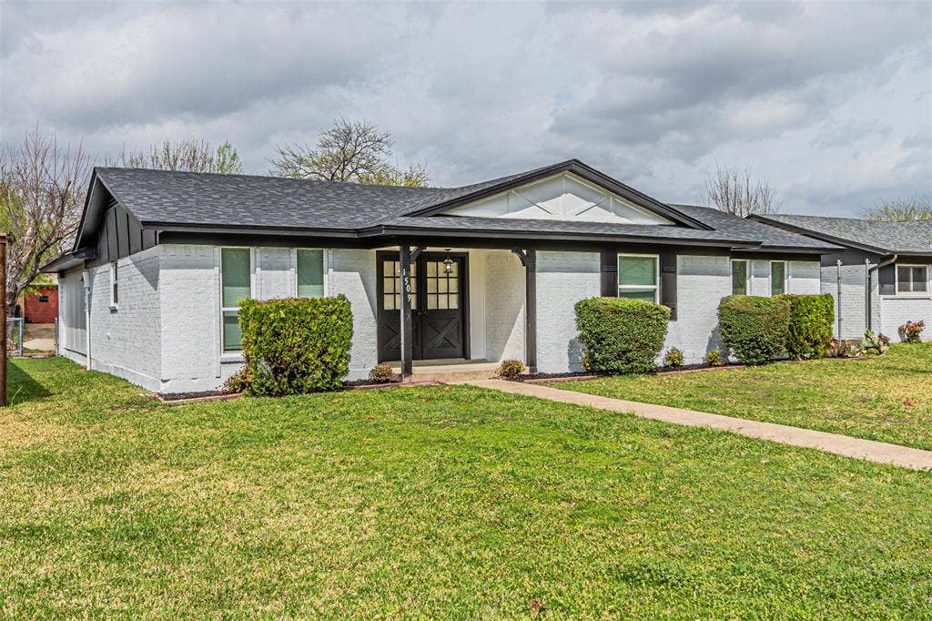 1509 Crockett Street, Garland, TX 75042 Single-story residence with a painted brick exterior, dark-trimmed gable roof, covered entryway, and double front doors
