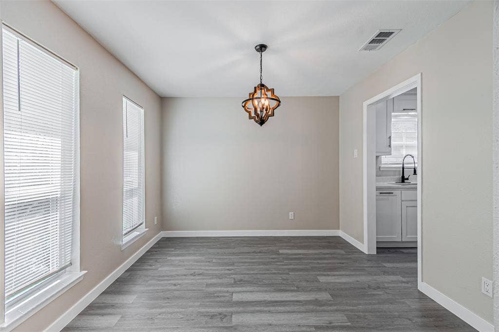 1509 Crockett Street, Garland, TX 75042 Neutral wall tones, wood-finish flooring, two large windows with blinds, and a multi-bulb lantern pendant fixture
