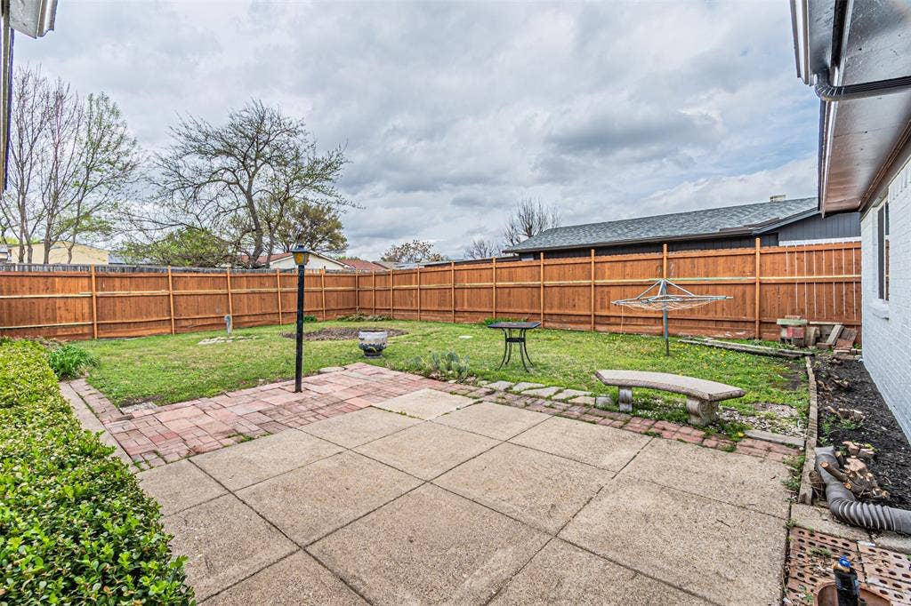 1509 Crockett Street, Garland, TX 75042 Backyard featuring a concrete patio, brick hardscaping, a wood privacy fence, and mature landscaping