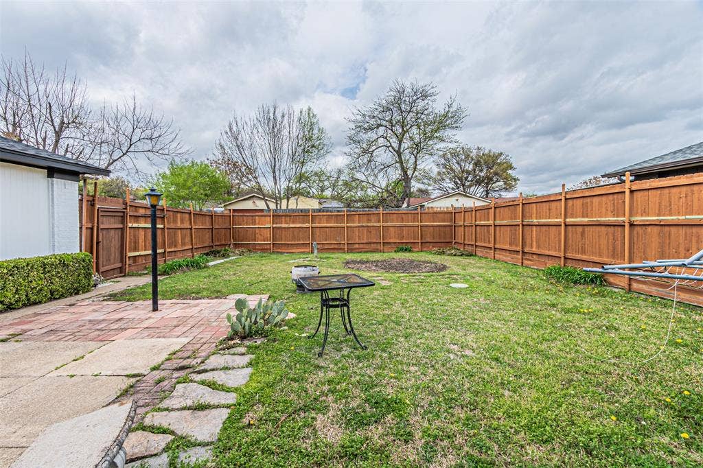 1509 Crockett Street, Garland, TX 75042 Backyard featuring a wood privacy fence, brick-paved patio, flagstone pathway, and grass lawn