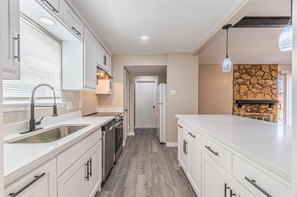 1509 Crockett Street, Garland, TX 75042 Kitchen featuring white shaker-style cabinetry, solid-surface countertops, wood-finish flooring, a high-arc pull-down faucet, and a stone-accented fireplace