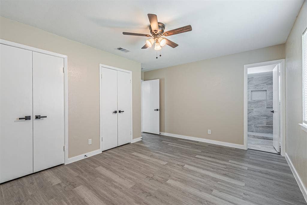 1509 Crockett Street, Garland, TX 75042 Room featuring wood-finish flooring, a ceiling fan with integrated lighting, dual closet doors with matte black hardware, and an entry to a tiled shower area