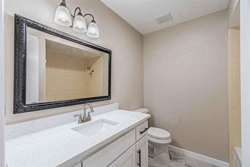 1509 Crockett Street, Garland, TX 75042 Bathroom featuring a vanity with a white countertop and rectangular undermount sink, black-framed mirror, three-light fixture, and tile shower surround