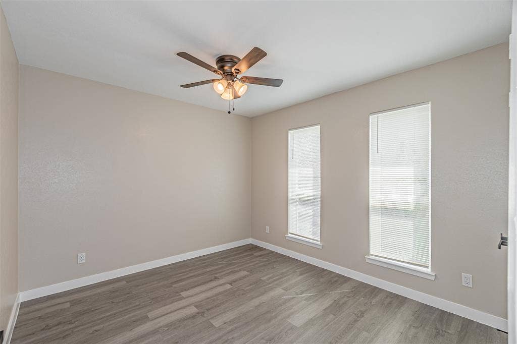 1509 Crockett Street, Garland, TX 75042 Neutral-toned interior space featuring wood-finish flooring, dual windows with integrated blinds, and a multi-light ceiling fan