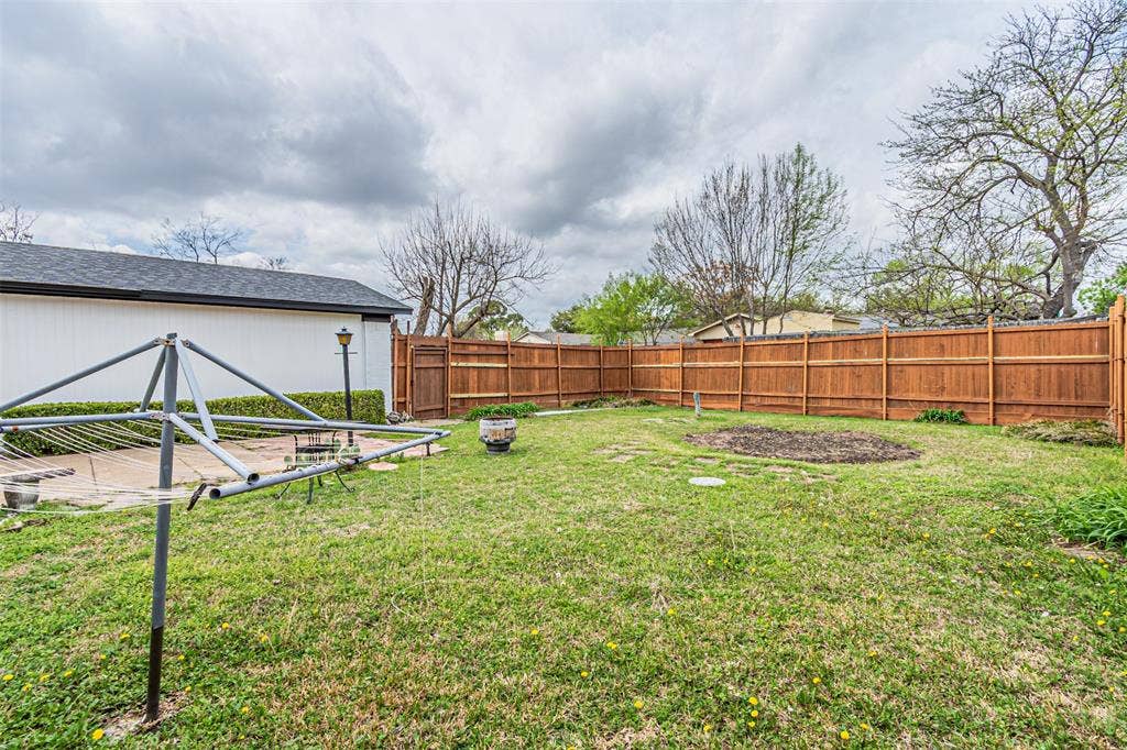 1509 Crockett Street, Garland, TX 75042 Backyard area featuring a wood-panel privacy fence, paved patio, and mature trees