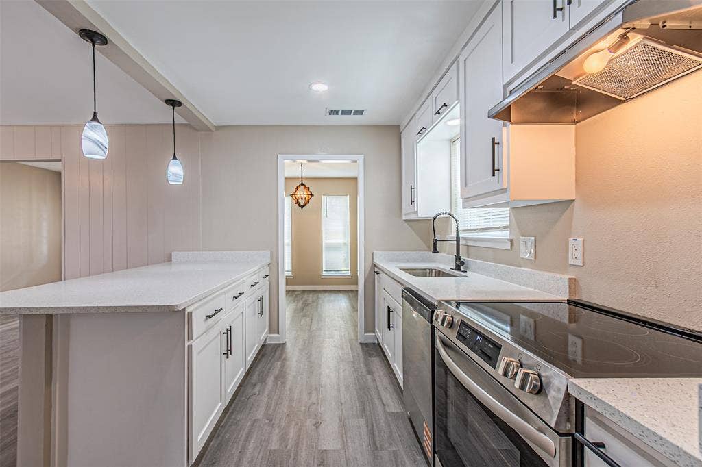 1509 Crockett Street, Garland, TX 75042 Kitchen featuring white shaker cabinetry, stone-finish countertops, stainless steel appliances, wood-finish flooring, and dual pendant lighting