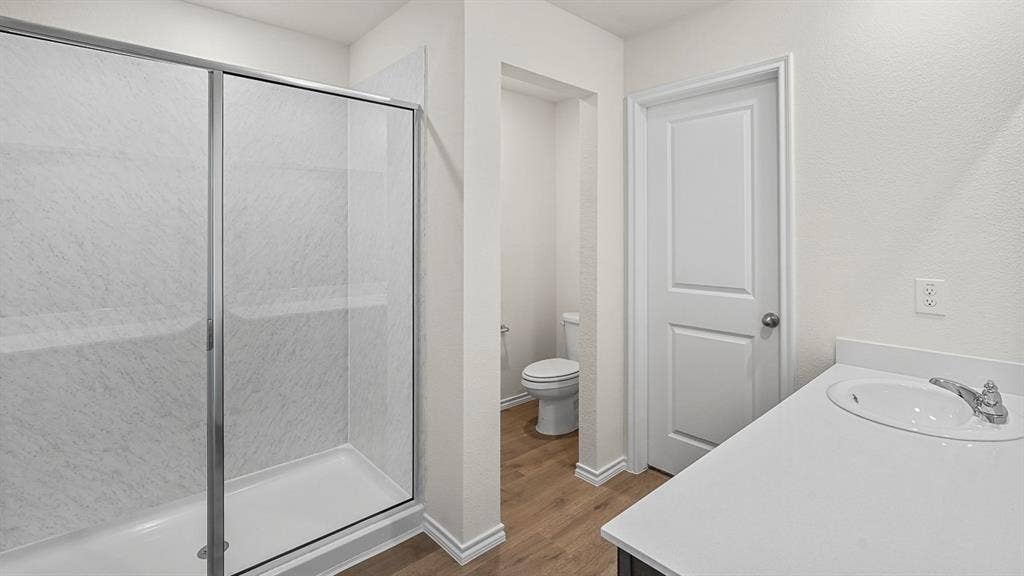 235 Whispering Pine Drive, Royse City, TX 75189 Shower featuring a glass sliding enclosure and stone-patterned surround, stone-surface vanity countertop with an integrated oval sink, and wood-finish flooring