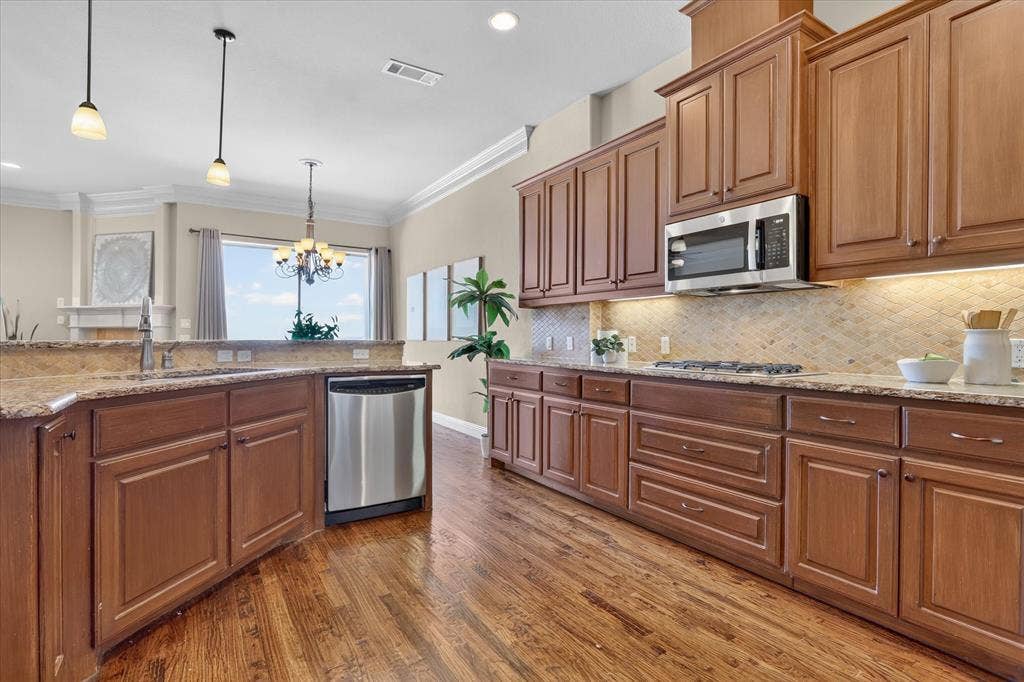 563 Rockingham Drive, Irving, TX 75063 Kitchen featuring wood cabinetry, stone countertops, stone tile backsplash, stainless steel appliances, and wood-finish flooring