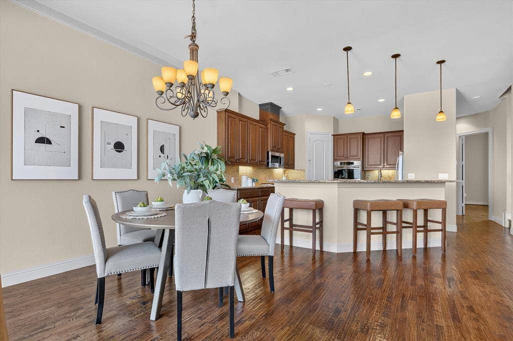 563 Rockingham Drive, Irving, TX 75063 Open-concept kitchen featuring stained wood cabinetry, stone countertops, integrated recessed lighting, metal pendant fixtures, and wood-finish flooring throughout the dining area