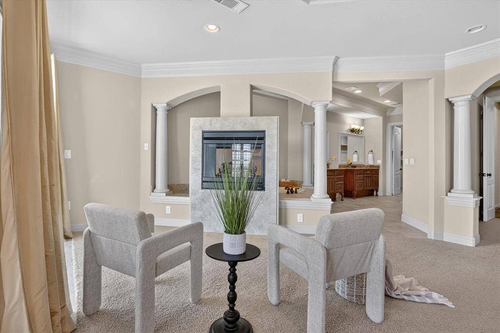 563 Rockingham Drive, Irving, TX 75063 Double-sided fireplace with light-toned stone surround, classical column detailing, crown molding, and recessed lighting