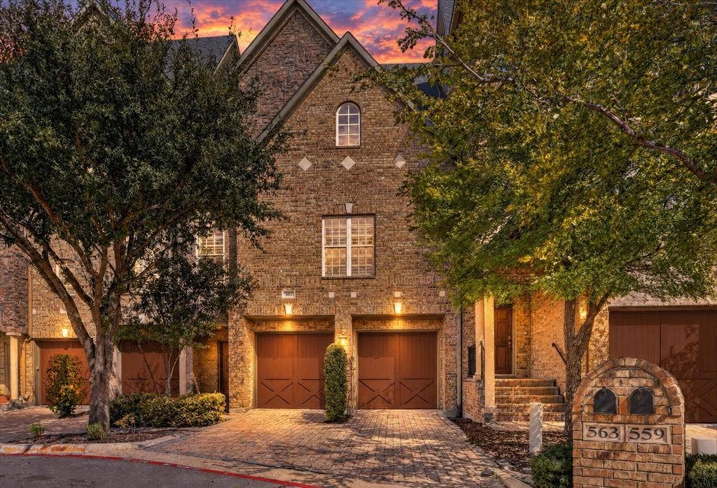563 Rockingham Drive, Irving, TX 75063 Multi-story brick exterior featuring an arched window, decorative stone accents, stone paver driveway, and carriage-style garage doors