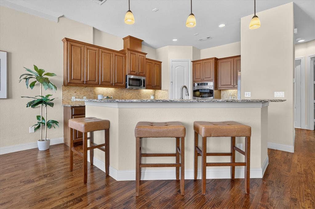 563 Rockingham Drive, Irving, TX 75063 Kitchen featuring wood cabinetry, stone countertops, a breakfast bar, recessed lighting, and stainless steel built-in appliances