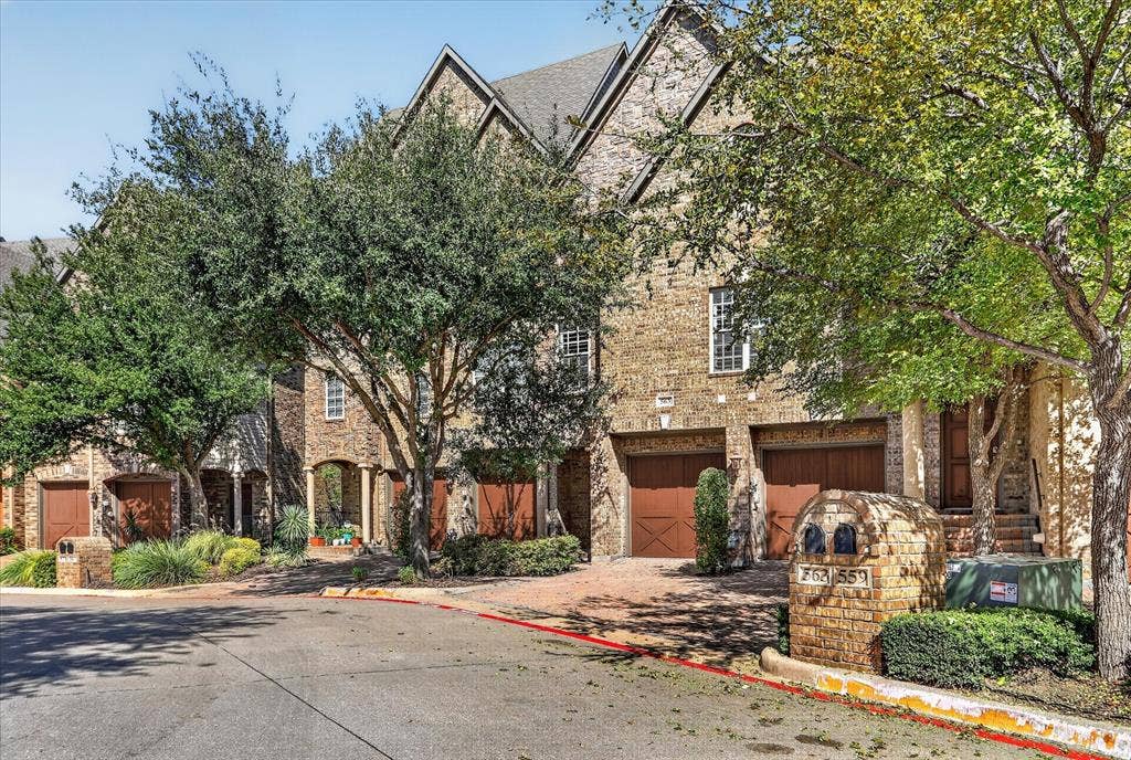 563 Rockingham Drive, Irving, TX 75063 Multi-story brick exterior featuring steep gabled rooflines, stone-accented mailbox columns, and wood-finish garage doors