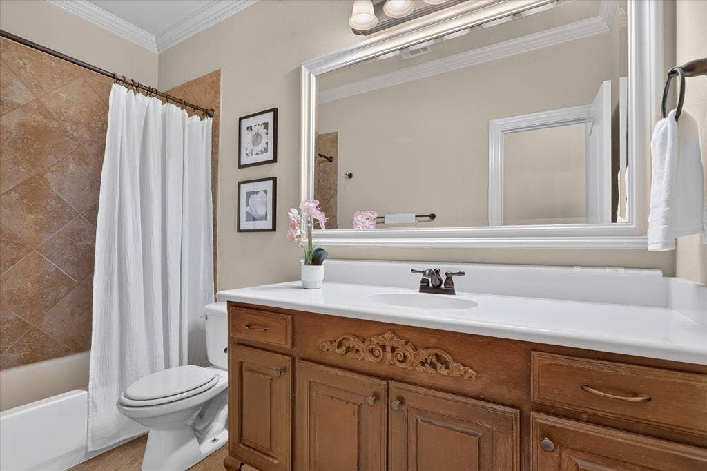 563 Rockingham Drive, Irving, TX 75063 Bathroom featuring a wood vanity with decorative millwork, a white integrated countertop sink, a large framed wall mirror, and a tub enclosure with tile surround