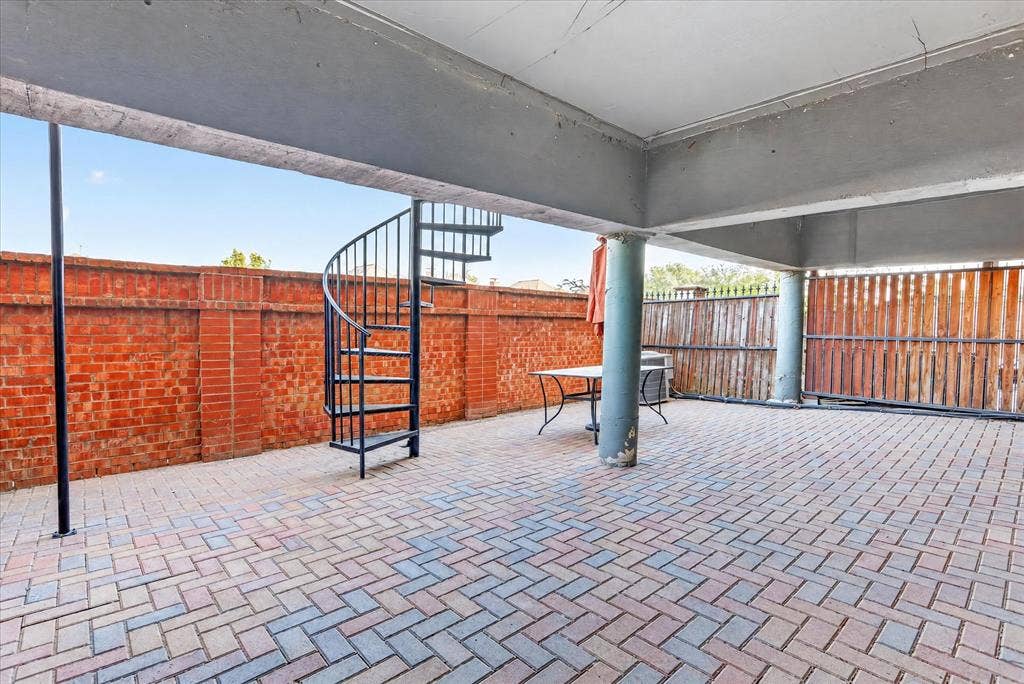 563 Rockingham Drive, Irving, TX 75063 Covered patio featuring herringbone-patterned brick pavers, a wrought-iron spiral staircase, structural concrete pillars, and a perimeter masonry wall