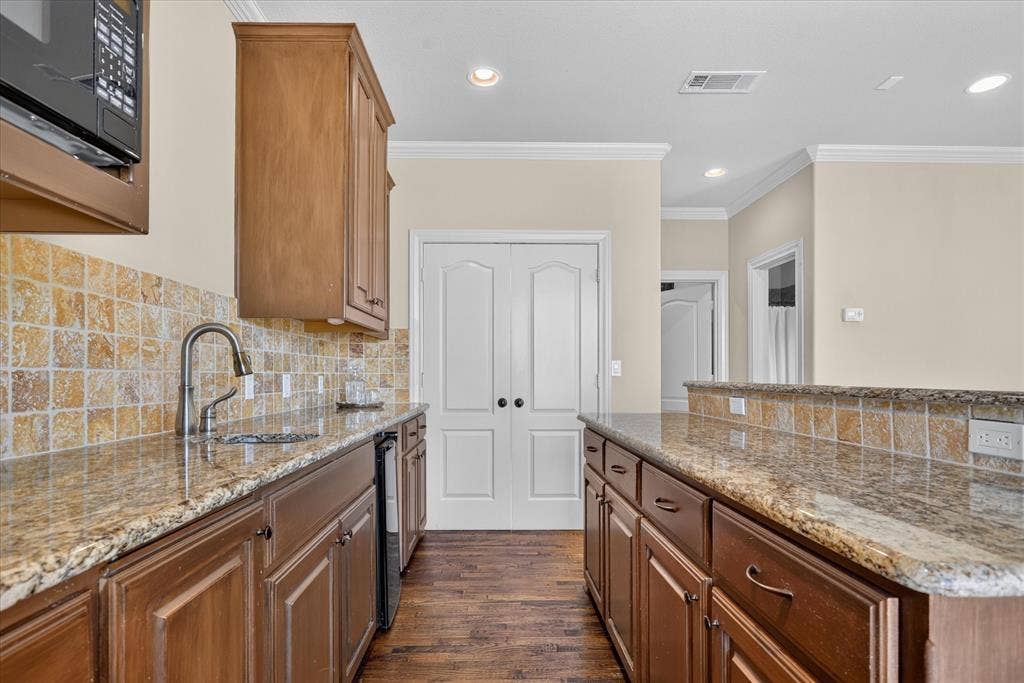 563 Rockingham Drive, Irving, TX 75063 Wet bar kitchen featuring wood cabinetry, granite countertops, square-tile backsplash, built-in microwave, mini sink, and mini fridge. Handscraped wood flooring throughout.