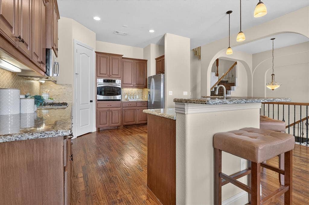 563 Rockingham Drive, Irving, TX 75063 Kitchen featuring wood-finish cabinetry, stone countertops, a stainless steel built-in oven, pendant lighting, and wood-finish flooring