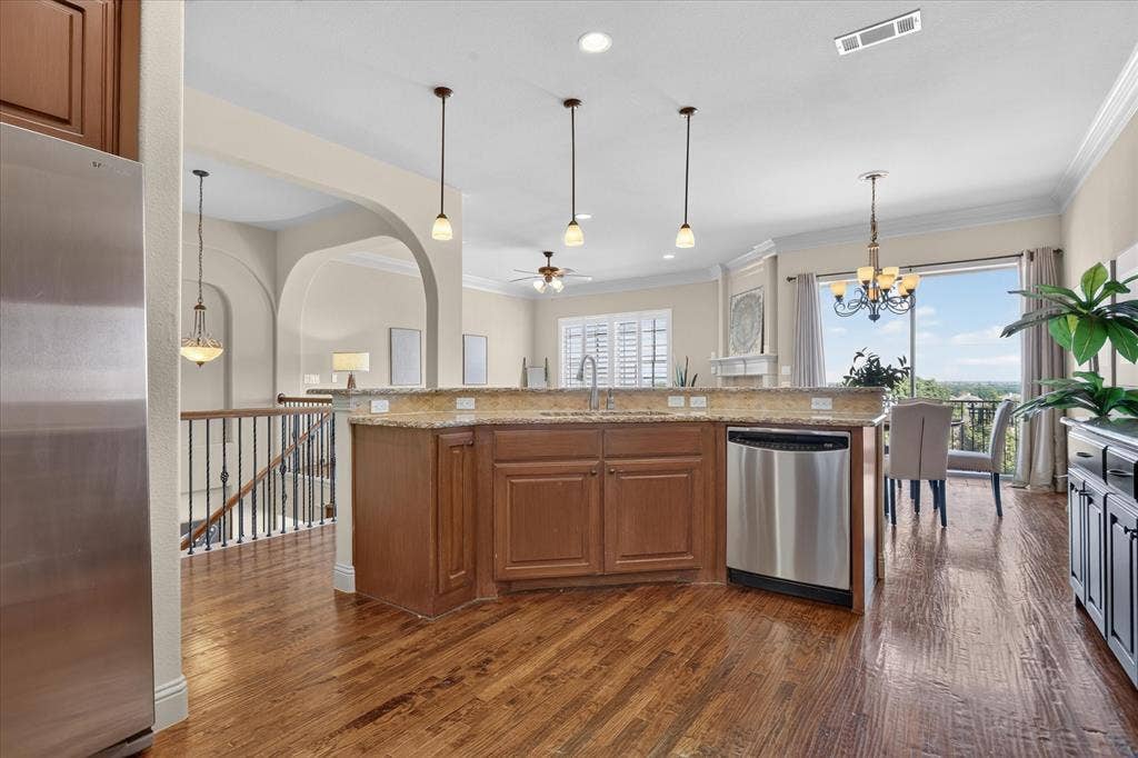 563 Rockingham Drive, Irving, TX 75063 Kitchen featuring wood-finish flooring, a stone-surfaced island with a stainless steel dishwasher, pendant lighting, arched architectural details, and decorative crown molding