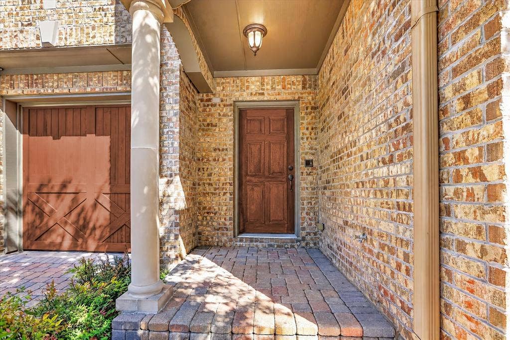 563 Rockingham Drive, Irving, TX 75063 Brick exterior featuring a covered entryway, a wood-finish multi-panel door, a classic column, and a stone-paver porch