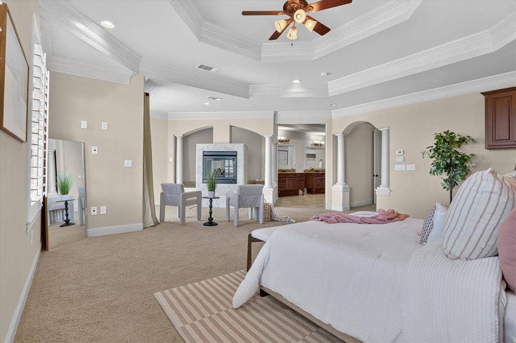 563 Rockingham Drive, Irving, TX 75063 Tray ceiling with recessed lighting and crown molding, gas fireplace with stone-finish surround, decorative columns, and plantation shutters