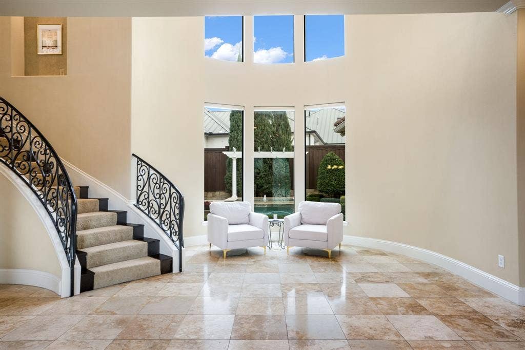 6590 Gerrard Street, Frisco, TX 75034 Grand foyer featuring soaring ceilings, a curved staircase with decorative wrought-iron railings, stone-tile flooring, and expansive windows