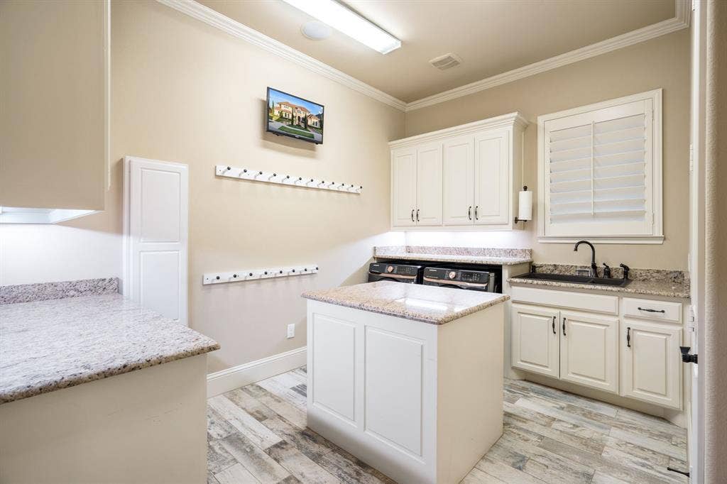 6590 Gerrard Street, Frisco, TX 75034 Utility room featuring white cabinetry, stone-finish countertops, a center island with prep space, an undermount sink with a matte black faucet, and wood-finish flooring