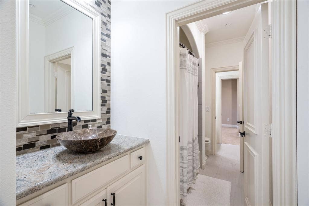6590 Gerrard Street, Frisco, TX 75034 Vanity featuring a stone-composite countertop, stone vessel sink, and matte black faucet, accented by a decorative linear glass-tile backsplash and framed mirror