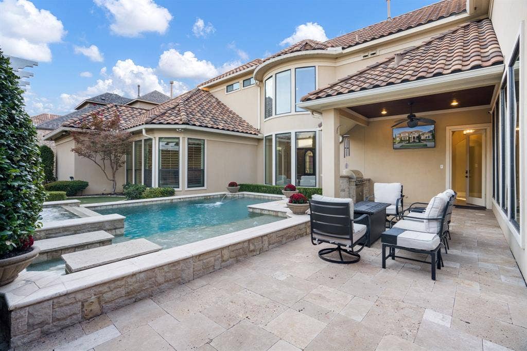 6590 Gerrard Street, Frisco, TX 75034 Outdoor living area featuring a covered patio, stone-tile flooring, an in-ground swimming pool with a raised stone-faced border, and a built-in outdoor kitchen station
