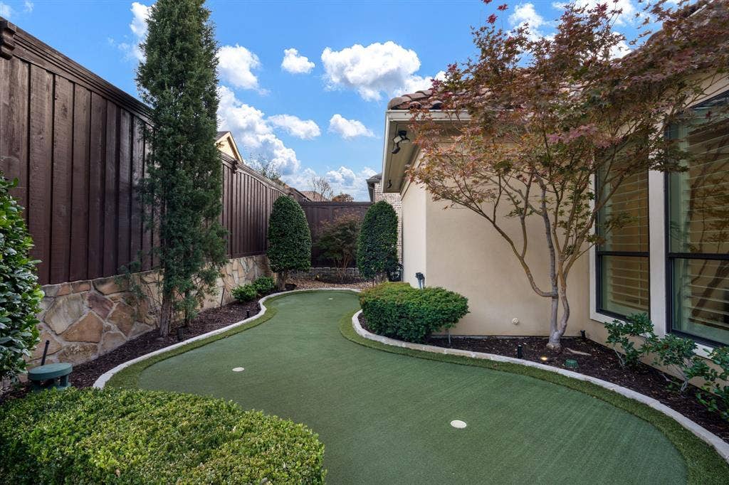 6590 Gerrard Street, Frisco, TX 75034 Backyard putting green featuring synthetic turf, stone-accented perimeter walls, vertical wood privacy fencing, and mature ornamental landscaping