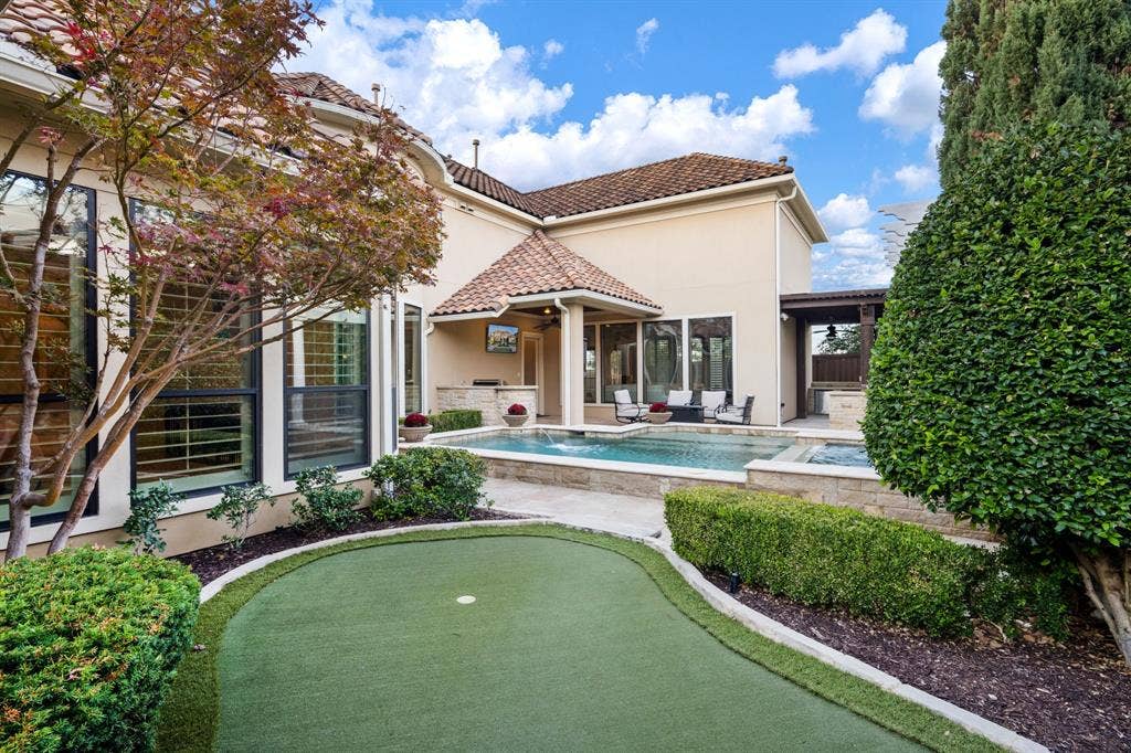 6590 Gerrard Street, Frisco, TX 75034 Stucco exterior featuring a tile roof, an in-ground pool with stone coping, a built-in outdoor kitchen, a synthetic turf putting green, and landscaped hedges