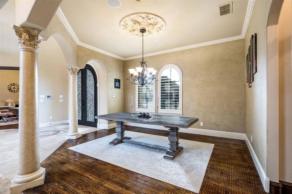 6590 Gerrard Street, Frisco, TX 75034 Formal dining area featuring decorative ceiling medallion, arched windows with plantation shutters, custom wrought iron entryway door, and architectural columns with ornate capitals