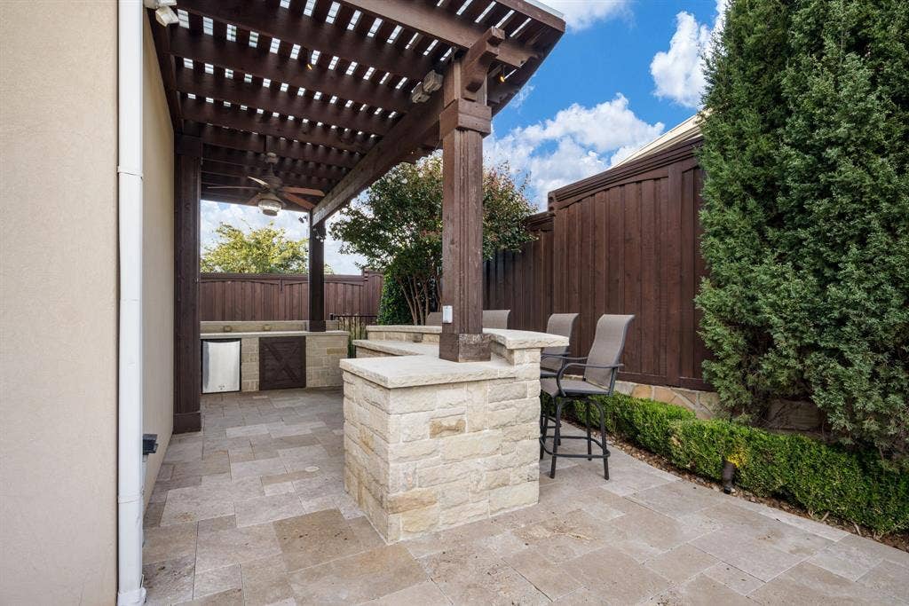 6590 Gerrard Street, Frisco, TX 75034 Outdoor living area featuring a covered pergola, stone-clad bar, built-in cabinetry, tile patio flooring, and stained wood privacy fencing