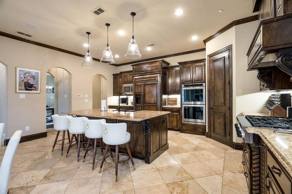 6590 Gerrard Street, Frisco, TX 75034 Kitchen featuring custom wood cabinetry, central island with stone countertop, built-in stainless steel double wall ovens, natural stone tile flooring, and decorative pendant lighting
