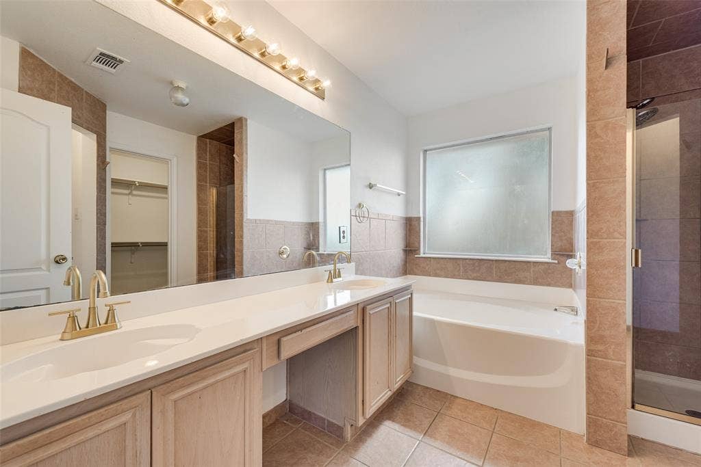 412 Overland Trail, Cedar Hill, TX 75104 Bathroom featuring a dual-sink vanity with light wood cabinetry, white countertops, brass-finish fixtures, a full-width mirror, and a tiled walk-in shower enclosure