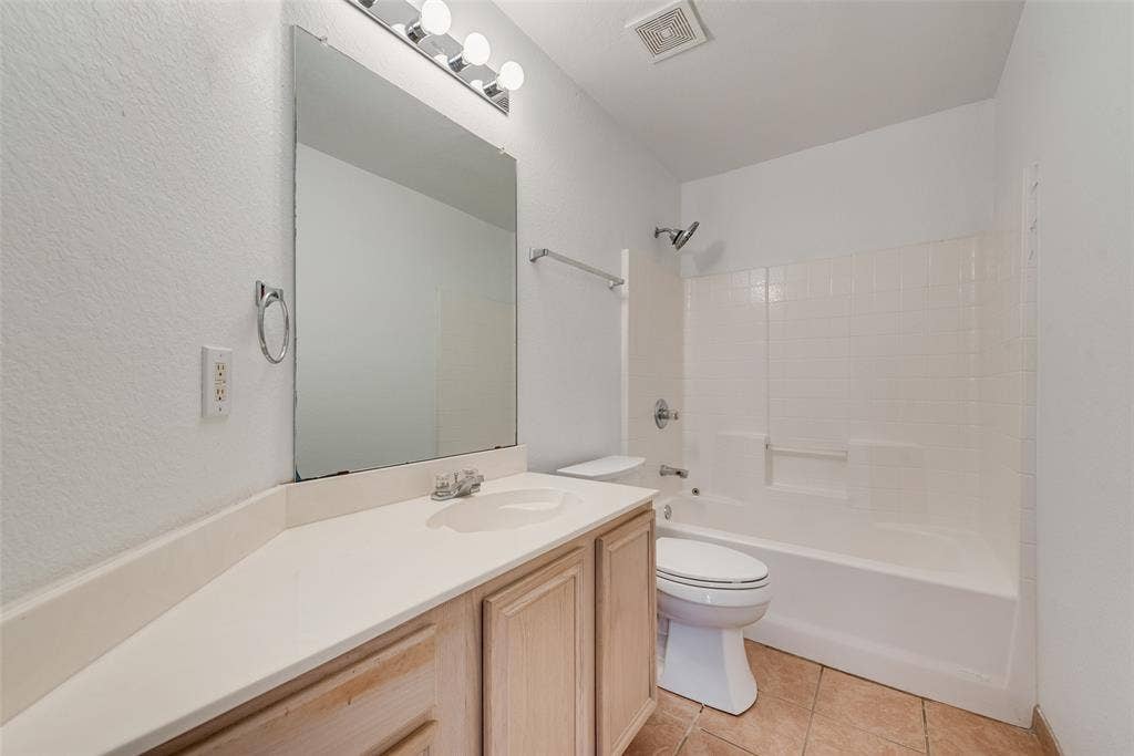 412 Overland Trail, Cedar Hill, TX 75104 Bathroom featuring a light wood-finish vanity, solid-surface countertop, full-height wall mirror, four-light vanity fixture, and a tiled shower surround