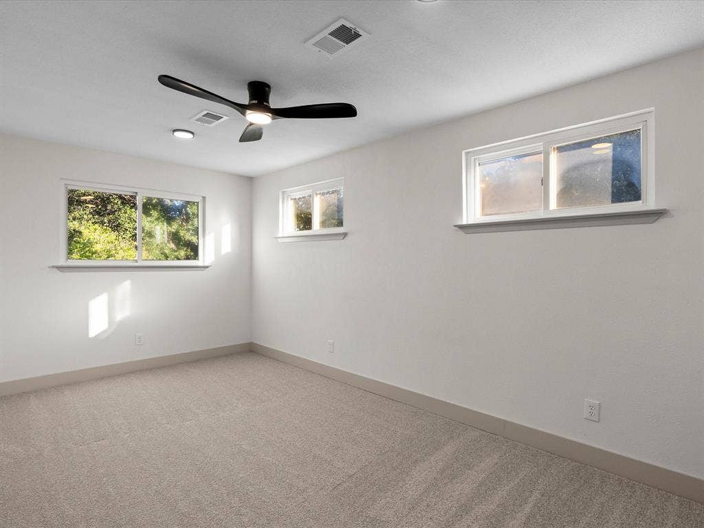 Neutral wall-to-wall carpeting, three sliding windows, and a matte black integrated ceiling fan with light