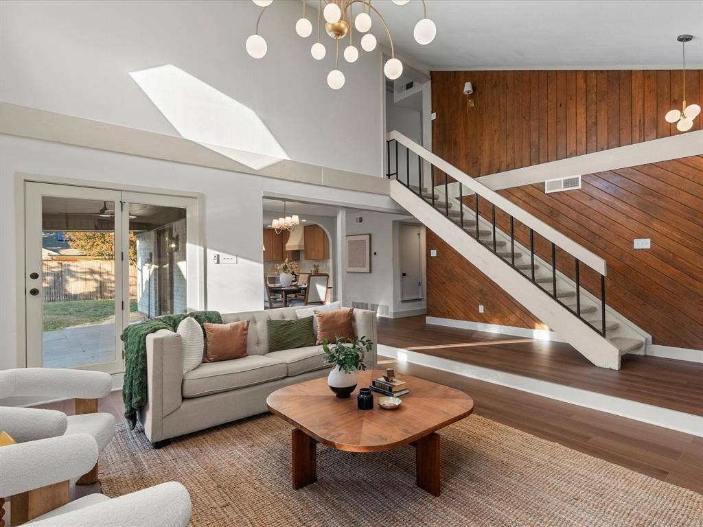 Vaulted ceiling with skylight, wood-paneled accent wall, wood-finish flooring, staircase with metal railing, and multi-light chandelier