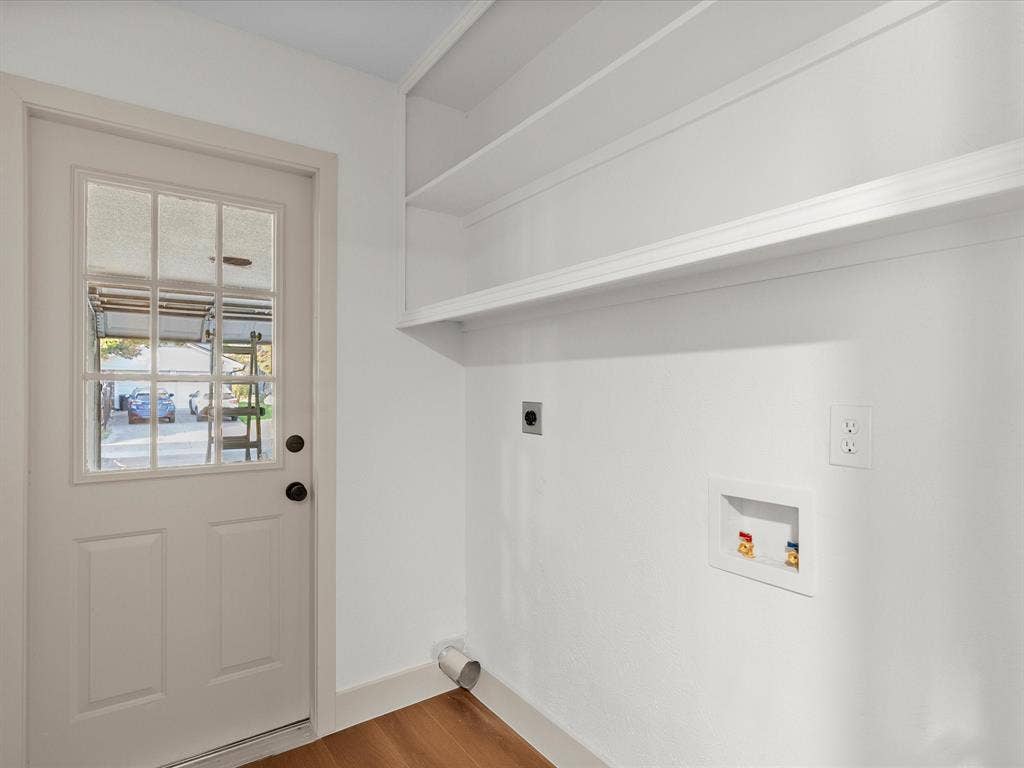 Service area featuring built-in wall shelving, laundry hookups, and a glass-paneled exterior door with wood-finish flooring