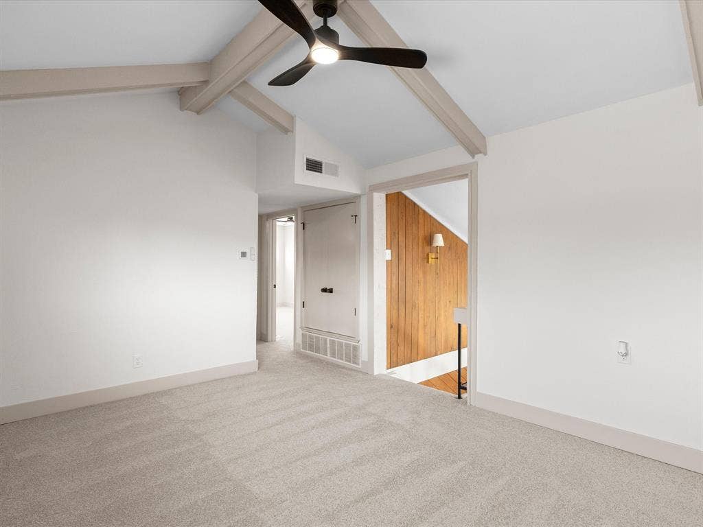 Vaulted ceiling featuring exposed beams, neutral carpeting, and a central ceiling fan with integrated lighting