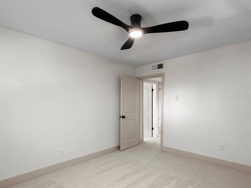 Neutral interior space featuring high-pile wall-to-wall carpeting, a matte black three-blade ceiling fan with integrated light fixture, and a solid-core paneled interior door with matte black hardware
