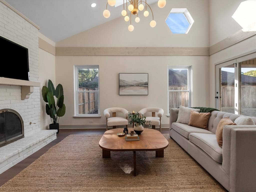 Vaulted ceilings featuring a chandelier with spherical pendants, white-painted brick fireplace, hexagonal skylights, and dark wood-finish flooring