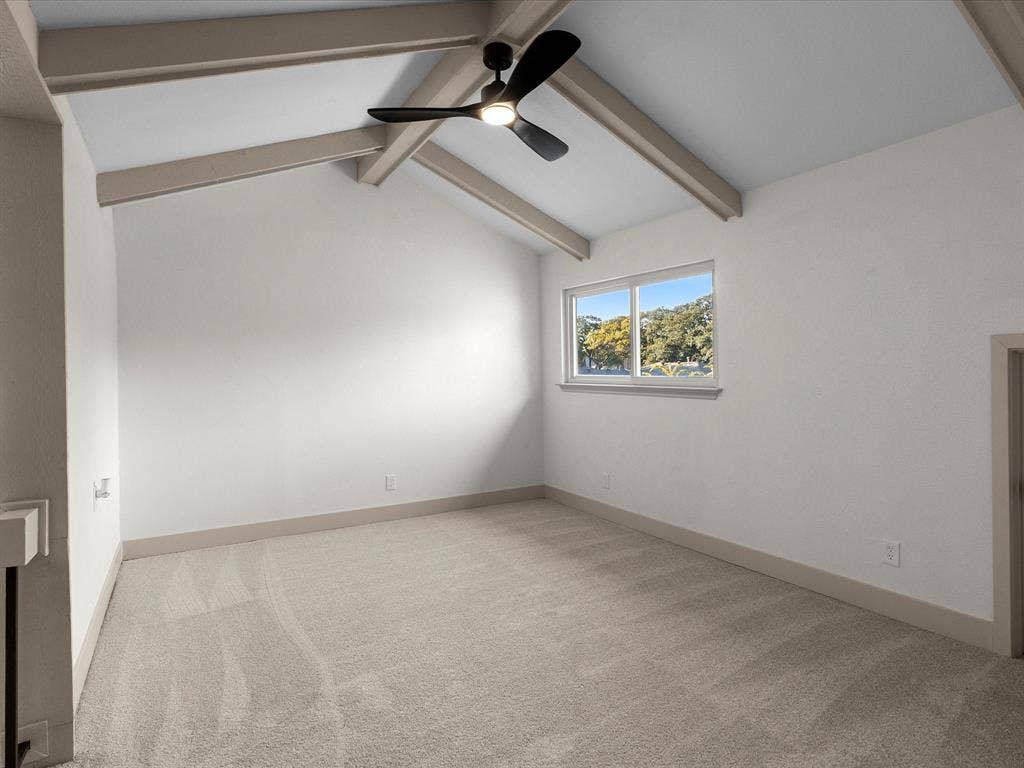 Vaulted ceiling featuring exposed beams, carpeted flooring, and a modern ceiling fan