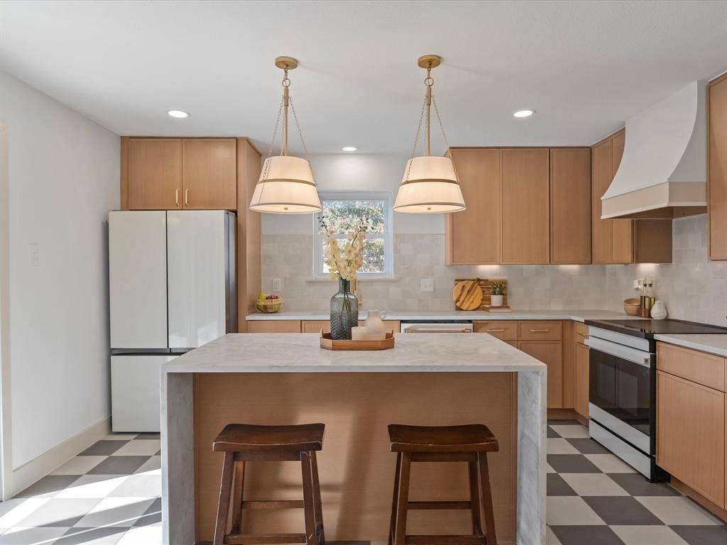 Kitchen featuring light-tone flat-panel cabinetry, waterfall island with stone countertop, custom range hood, and checkerboard tile flooring
