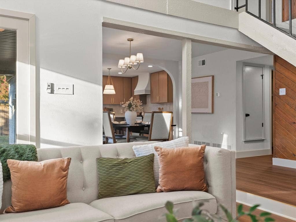 Arched entryway featuring a neutral color palette, wood-finish flooring, vertical wood plank wall paneling, multi-arm chandelier lighting, and a staircase with metal railings