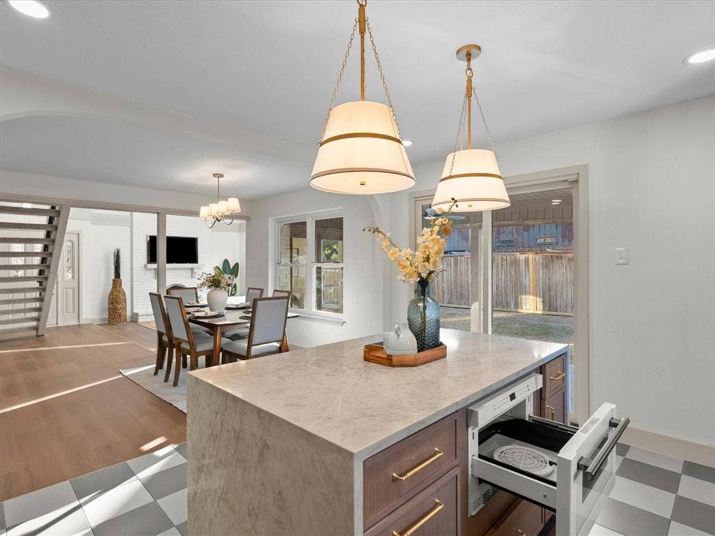 Center island featuring stone-finish countertop, built-in microwave drawer, and wood-finish cabinetry with brass-tone hardware, accented by dual pendant lights